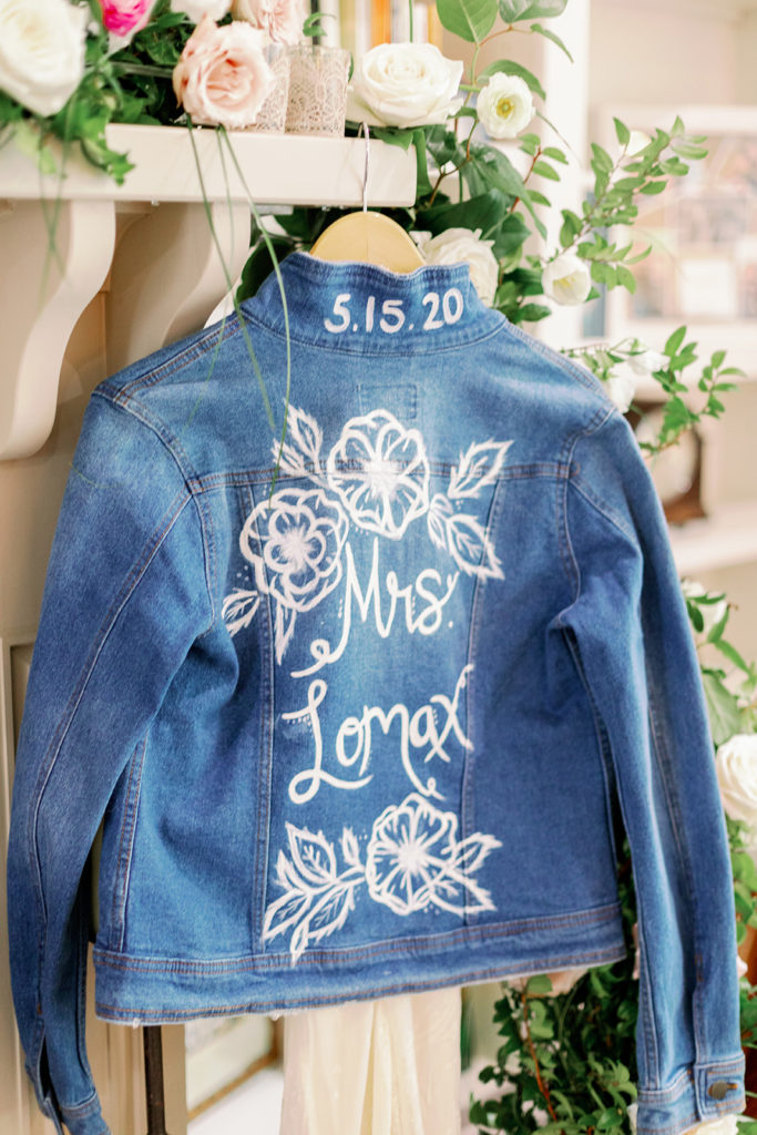 A jean jacket painted with white florals, "Mrs. Lomax," and the wedding date (5.15.20). 