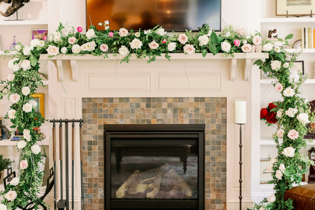 The mantle of the couple's home is adorned with a garland of greenery and pink and white florals. 