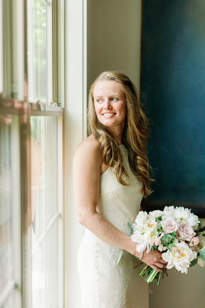 The bride smiles in her lace gown with her bouquet. 