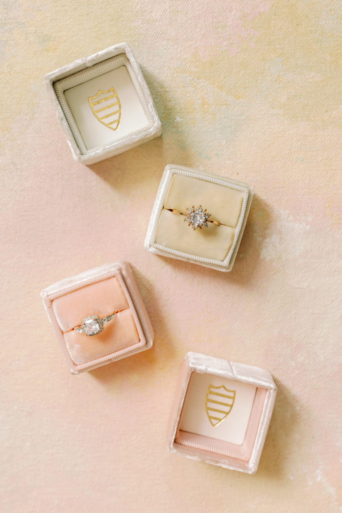 Ring boxes are displayed on a pink ombre background. 