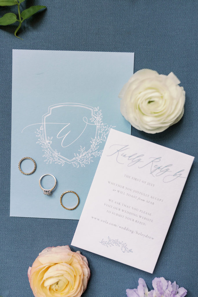 The wedding rings are displayed on the invitation suite, designed in colors of blue and white, against a darker blue background. 